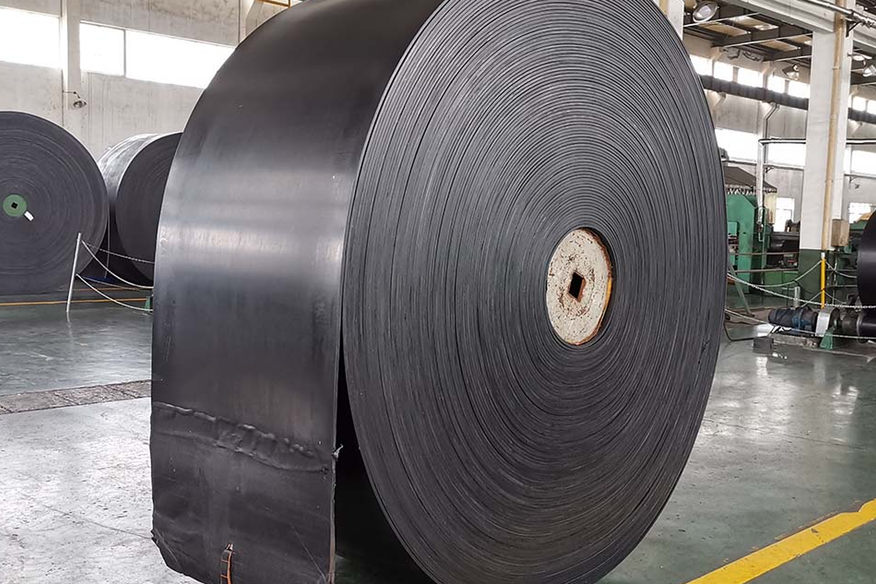Taller de fabricación de cintas transportadoras SINOCONVE con gran rollo de cinta terminada y línea de producción