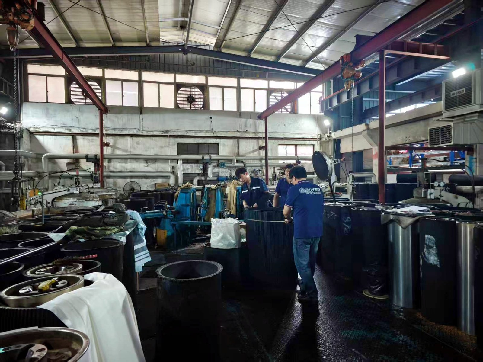 Trabajadores operando maquinaria industrial y grandes cilindros en una fábrica de correas.