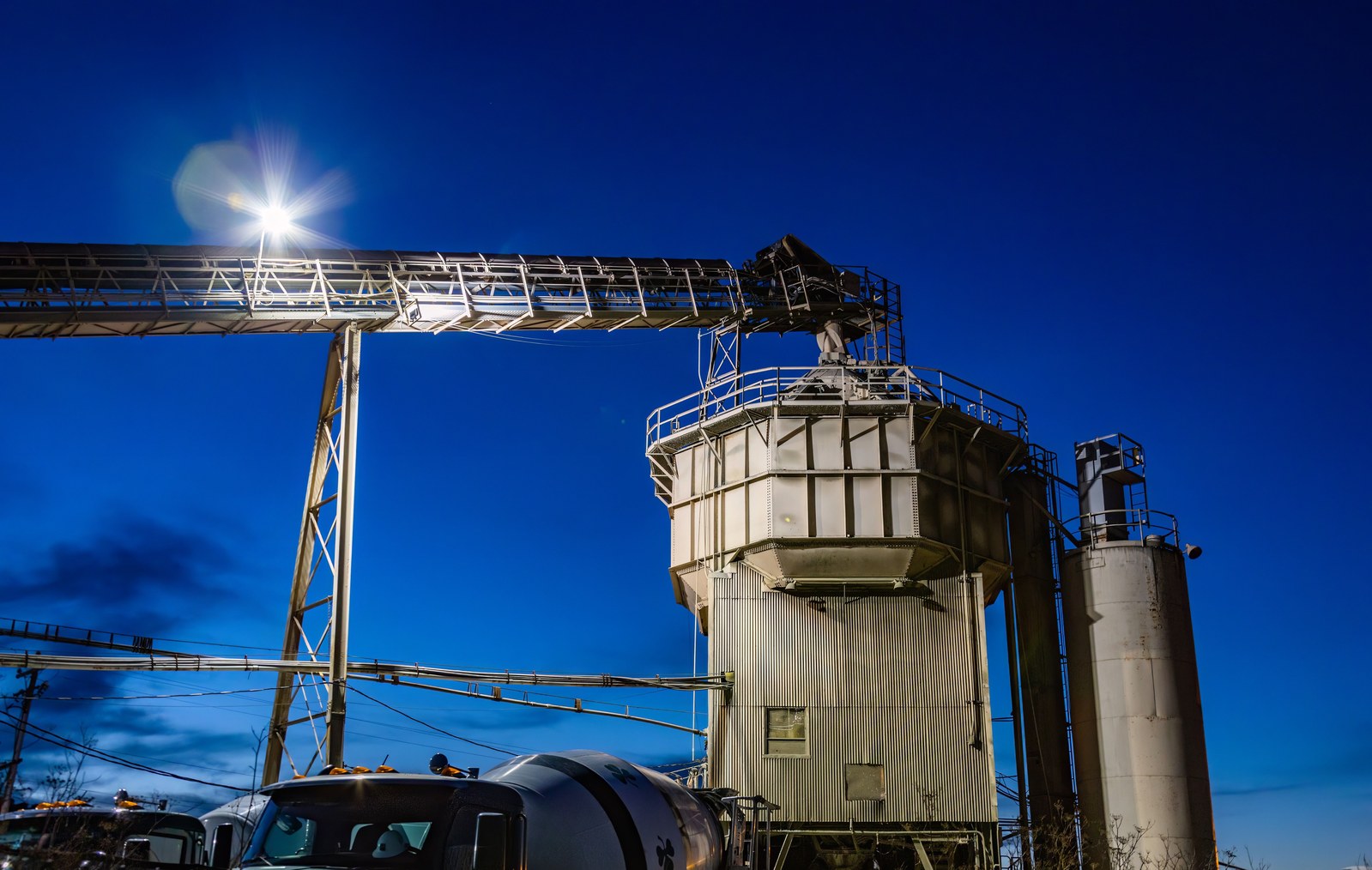 Planta de dosificación de hormigón que opera de noche con silos y cintas transportadoras.