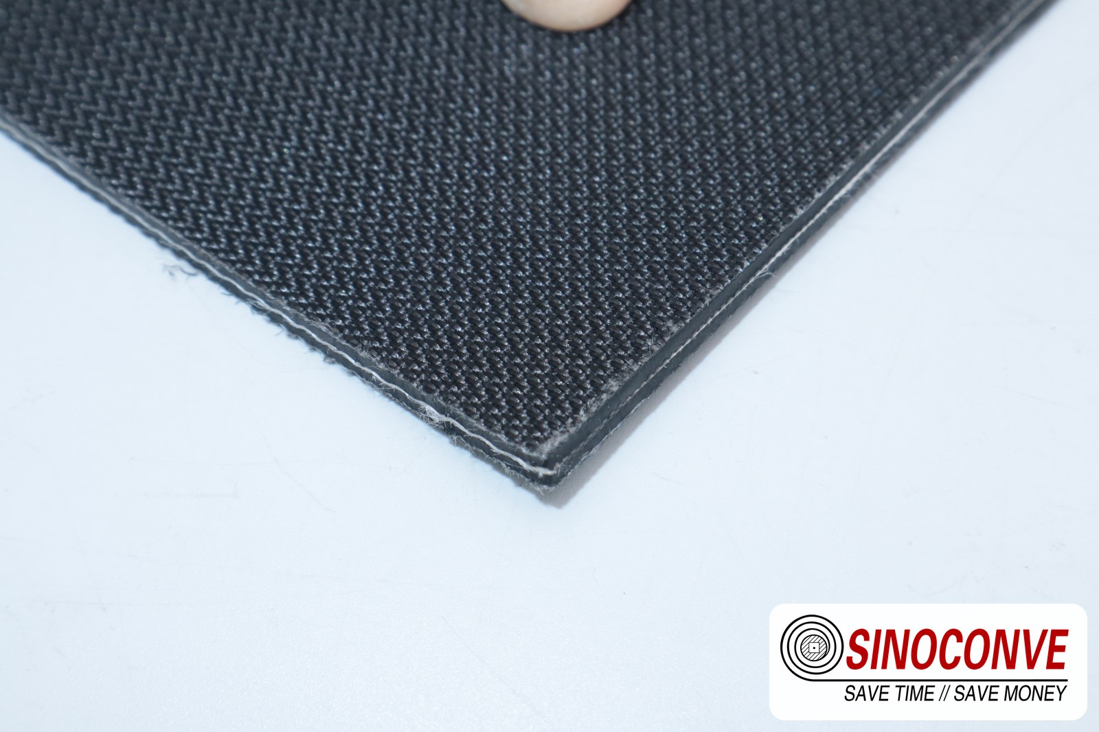 Cut edge of a black rough-top wood panel conveyor belt showing cover thickness for press line duty