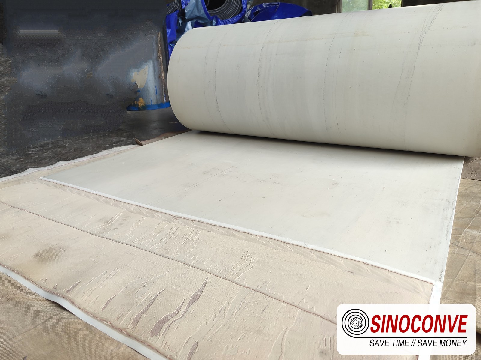 Roll of white food-grade malt conveyor belt unrolled across a plant floor for inspection before installation